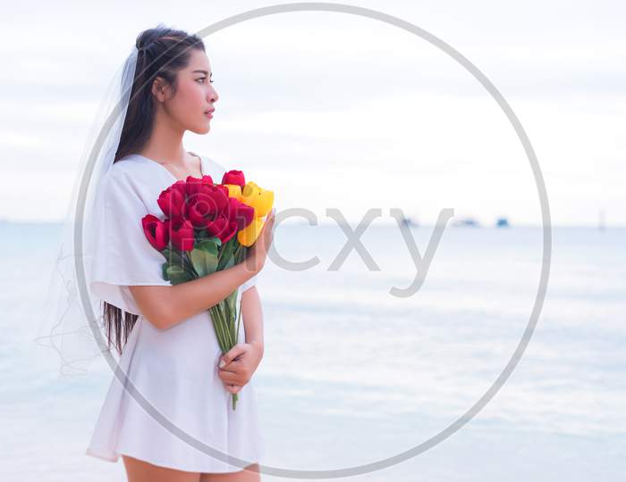 Asian Woman Holding Flowers And Waiting For Someone Make Her Happy. Lonely And Single Woman Concept. Sadness And Destiny Concept. Beauty And Nature Theme. Ocean And Sea Theme. Finding Soulmate Theme.