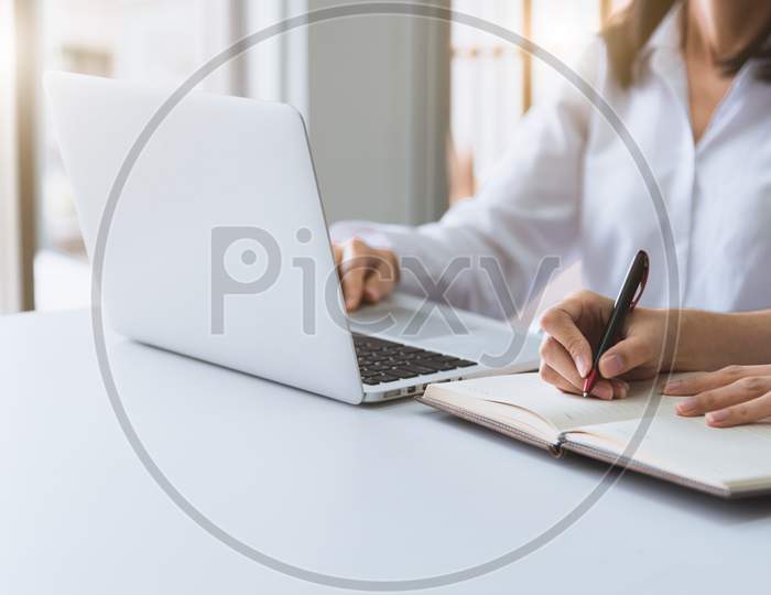 Close Up Of Two Businesswoman Using Laptop And Writing On Notebook In The Morning. Business And Financial Concept. People And Lifestyles Concept. Office And Workplace Theme.