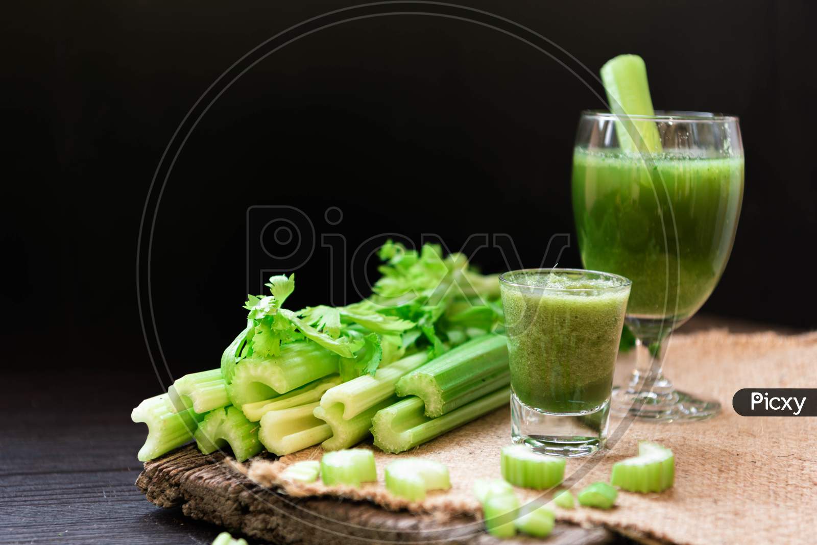 Blended Celery Juice In Welcome Drink Glass And Bunch Of Fresh Celery Stalk On Wooden Table With Leaves On Black Background. Food And Ingredients  Of Healthy Vegetable. Freshness Herbal For Dieting