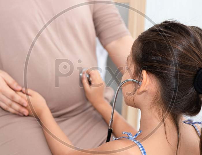 Cute Daughter Listens To Voice Of Baby In Mother Belly For Checking. Pregnant And Parents. Health And Medical. People Lifestyles And Family Concept.