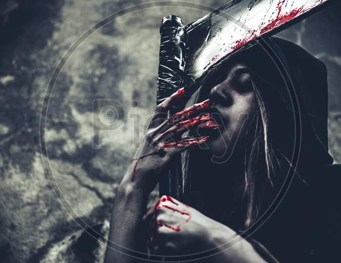 Witch Licking Blood On Fingers. Female Demon Angel In Black Clothes And Hood On Grunge Wall Background. Halloween Day And Mystery Concept. Fantasy Of Magic Theme. Afterlife And Death Concept.