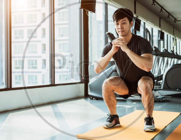Sport Man Doing Squat Posture On Yoga Mat In Fitness Gym At Condominium In Urban. People Lifestyles And Sport Workout Concept.