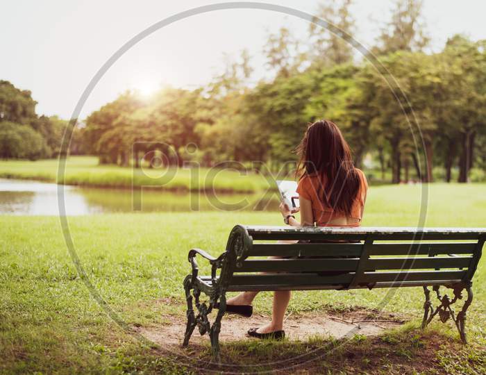 Back View Of Happy Beauty Woman In Casual Outfits Using Tablet In National Park Background. People Lifestyles And Technology Concept. Nature And Relaxation Theme. Summer And Autumn Seasonal Theme.