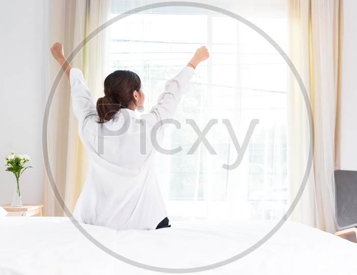 Back View Of Woman Stretching In Morning After Waking Up On Bed Near Window. Holiday And Relax Concept. Lazy Day And Working Day Concept. Office Woman And Worker In Daily Life Theme
