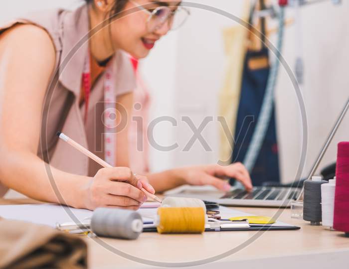 Attractive Asian Female Fashion Designer Working In Home Office Workshop. Stylish Fashionista Woman Creating New Cloth Design Collection. Tailor And Sewing. People Lifestyle And Occupation Concept