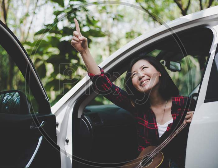 Beauty Asian Woman Pointing And Having Fun At Outdoors Summer With Ukulele In White Car. Traveling Of Photographer Concept. Hipster Style And Solo Woman Theme. Lifestyle And Happiness Life Theme.