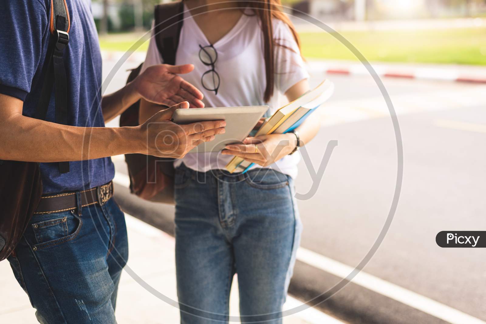 Close Up Of Two College Student Discussion With Tablet. Girl Holding Books Talking To Boy In University Or School. Education And Lifestyle Learning. Technology And Self Learning Concept