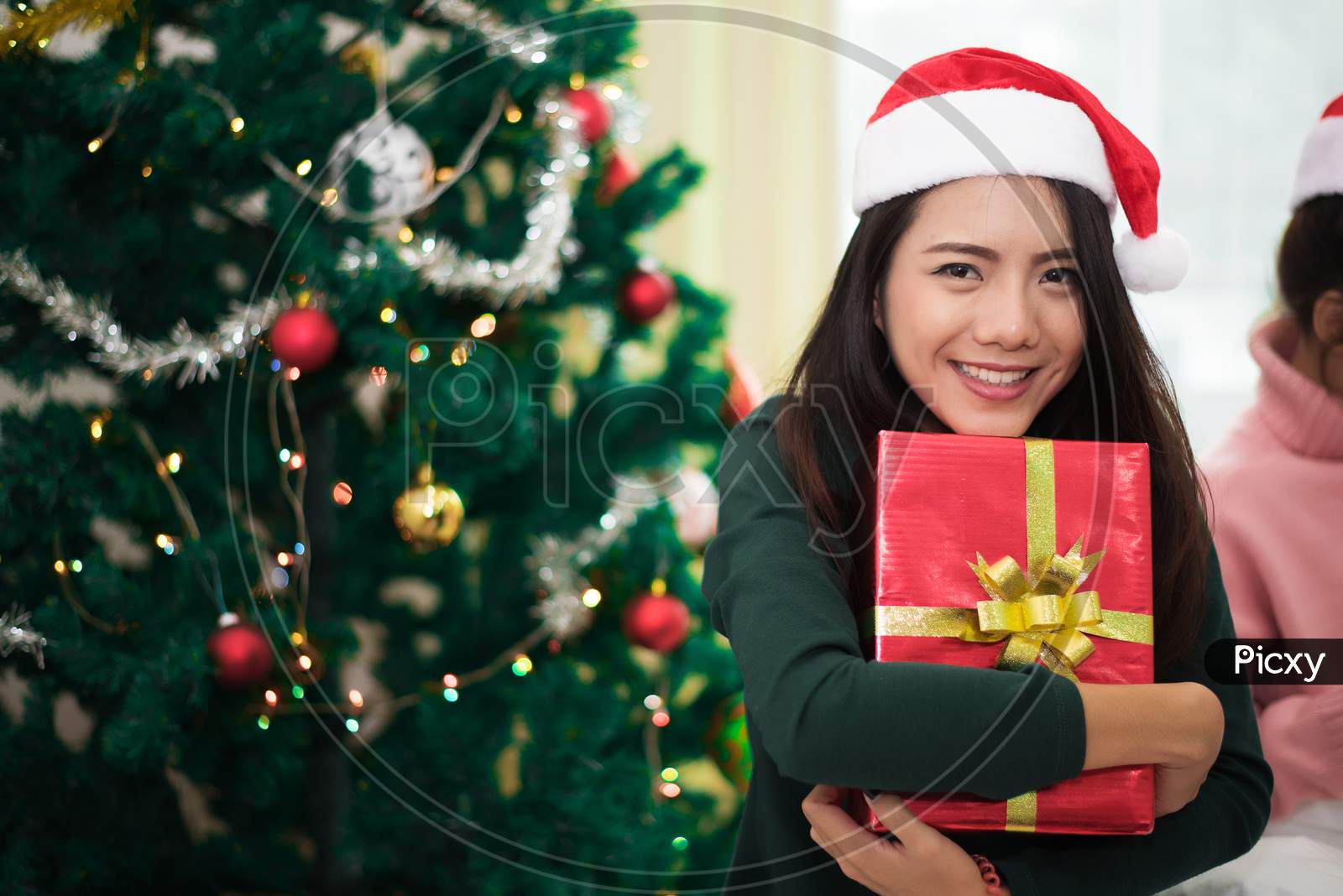 Asian Woman Holding A Gift Or Present With Christmas Tree And Decor. Xmas And New Year Concept. Holiday Theme