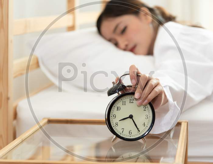 Asian Young Beauty Woman Turning Off Alarm Clock In Morning Late Without Looking Clock And Lazy To Working On In Holiday. Bedroom And Bed Time Concept. Relaxation And People Lifestyles Of Tired Worker
