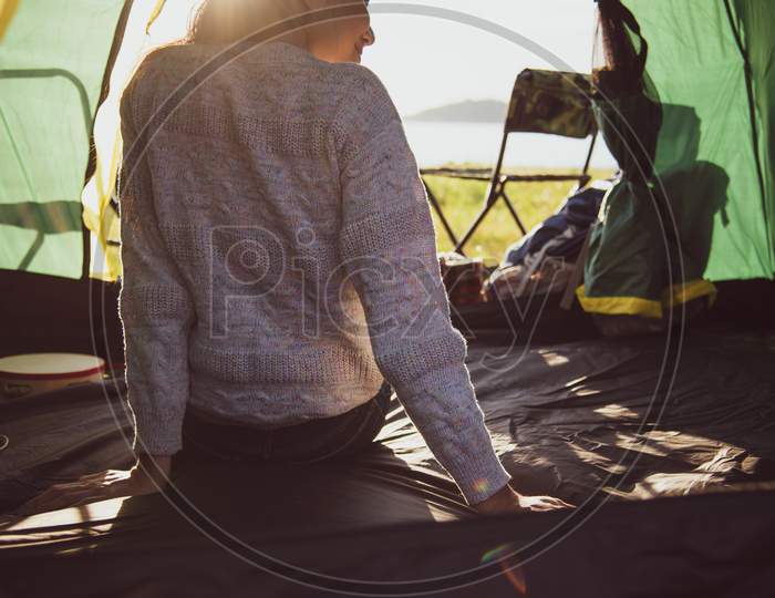 Back View Of Happy Female Tourist Relaxing In Camping Tent With Mountain And Sun Flare Background. People And Lifestyles Concept. Travel And Vacation In Outdoors Meadow. Tourism And Hiking Theme.