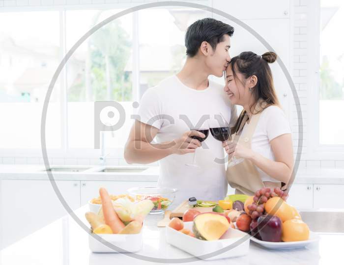 Asian Lovers In Kitchen, Man Give Forehead Kiss To Woman While Clink Wine Glasses To Each Other. Family And Couple Concept. Honeymoon And Holidays Theme