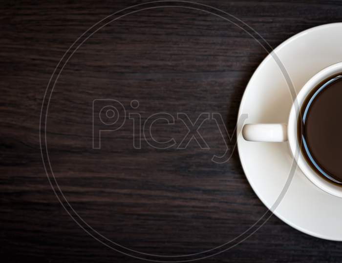White Coffee Cup On Wood Table Background With Copy Space, Half Cup With Full Of Coffee, Dark Tone Still Life And Vignette, Top View For Advertisement, Business And Drinking Concept, Relax Concept