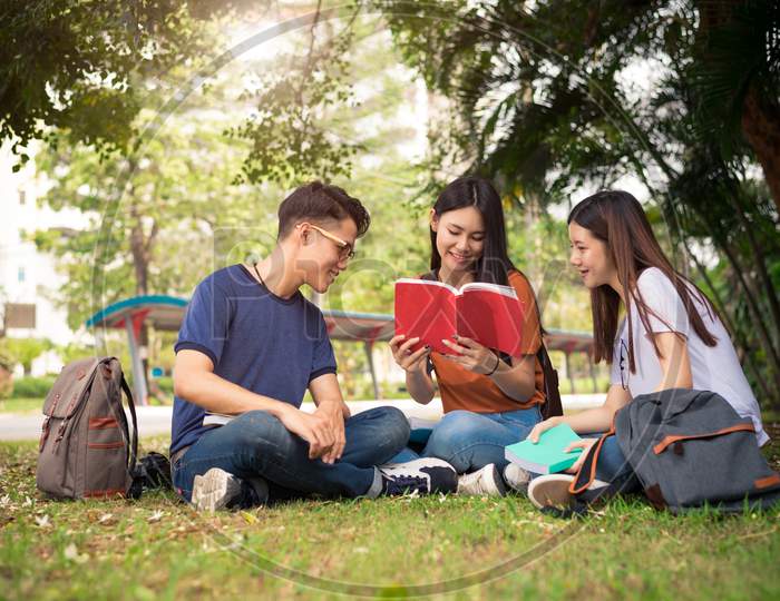 Group Of Asian College Student Reading Books And Tutoring Special Class For Exam On Grass Field At Outdoors. Happiness And Education Learning Concept. Back To School Concept. Teen And People Theme.