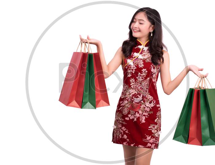 Young Asian Beauty Woman Wearing Cheongsam And Holding Red And Green Shopping Bags Gesture In Chinese New Year Festival Event On Isolated White Background. Holiday And Lifestyle Concept. Qipao Dress