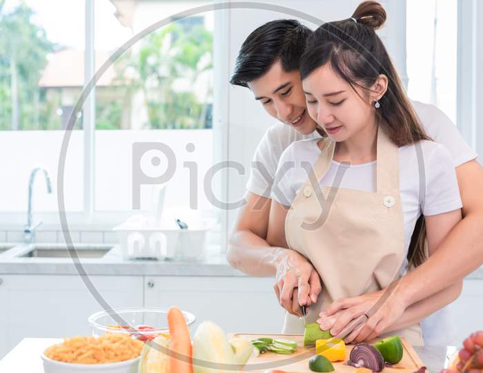 Asian Couples Cooking And Slicing Vegetable In Kitchen Together. Man Teaching Woman To Preparing Meal In Home. People And Lifestyles. Holiday And Honeymoon Concept. Valentine Day And Wedding Theme