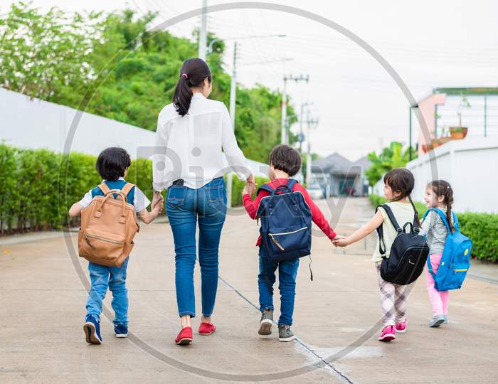 Group Of Preschool Student And Teacher Holding Hands And Walking To Home. Mom Bring Her Children Go To School Together. Back To School And Education Concept. People And Lifestyles Theme. Back View