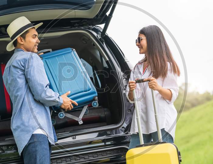 Asian Man Helping Woman To Lifting Suitcase From Car During Travel In Long Weekend. Couple Have Road Trip In Vacation With Yellow Luggage. People Lifestyle And Transportation Concept. Nice Guy Theme