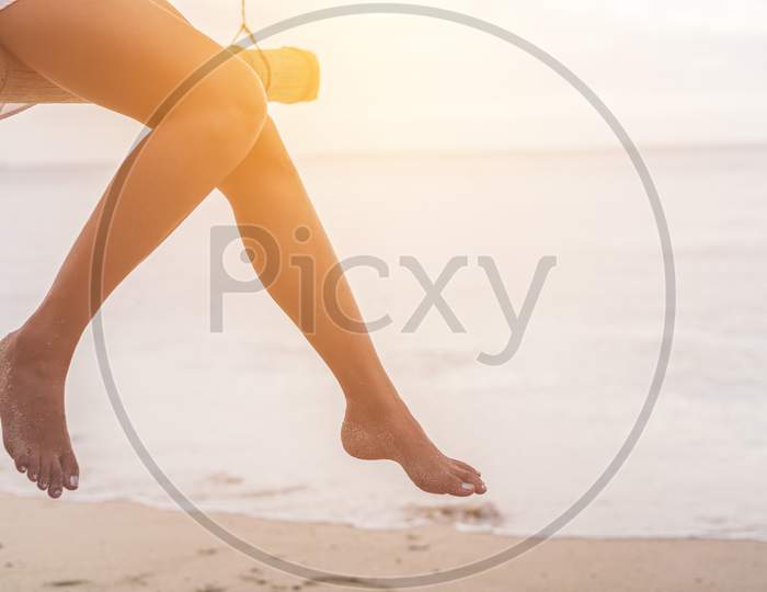 Woman Legs At Beach On Wooden Swing. Relax And Single Woman Concept. Happiness And Lifestyle Concept. Lonely And Sadness Concept. Beach And Sea Theme. Finding Soulmate Theme. Copy Space On Right