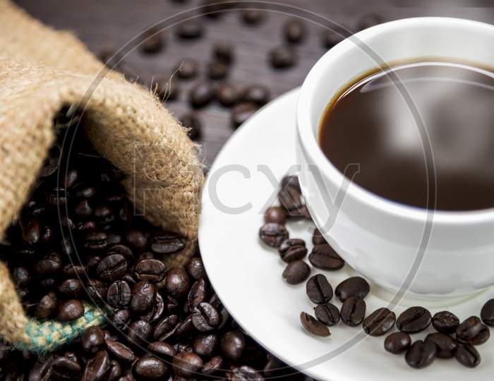 Coffee Cup With  Smoke And Coffee Beans In Sack On Wood Table, Drinks And Relax Concept, For Advertising