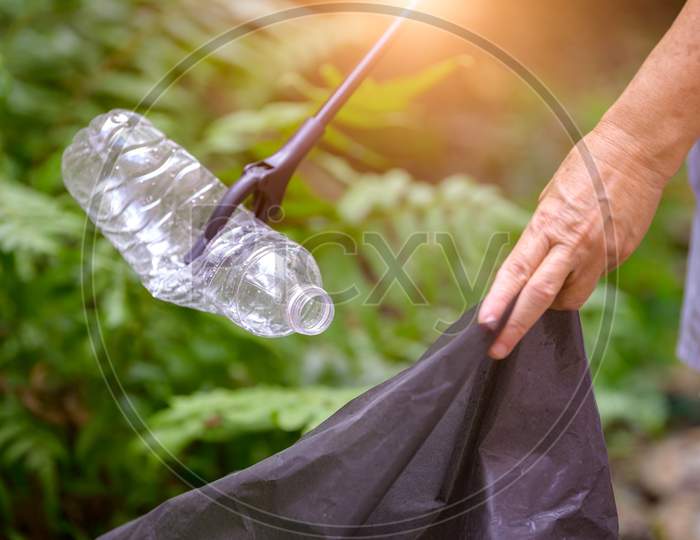 Closeup Of Hand And Waste Grabber Picking Up Drinking Plastic Bottle Waste Into Bag. Ecology And Environmental Concerns. Recycling Waste Reduction Techniques. Eco-Friendly Earth World Disaster Relief