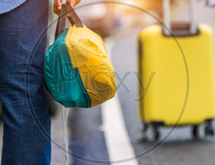Closeup Of Tourist Legs Walking Along Road With Bag During Travel In Countryside. People Lifestyles And Vacation Concept. Man Holding And Backpacking For Long Holiday Trip With Mountain Background