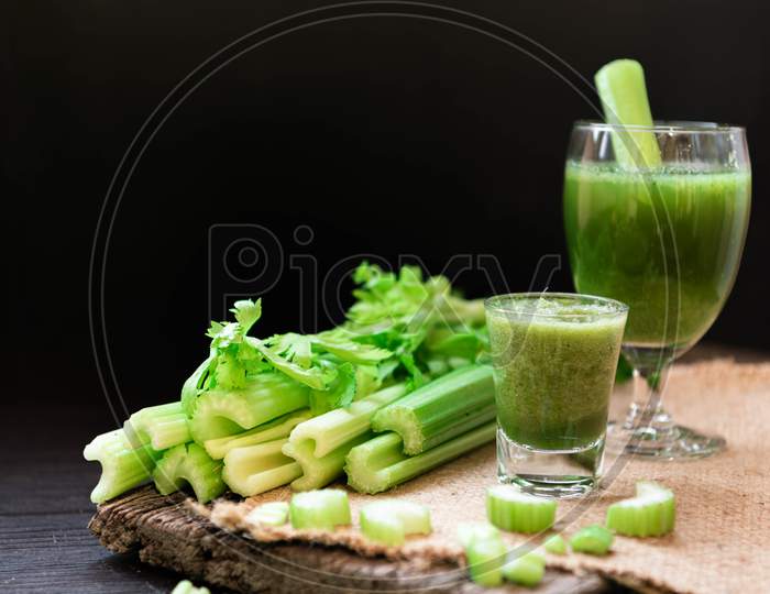 Blended Celery Juice In Welcome Drink Glass And Bunch Of Fresh Celery Stalk On Wooden Table With Leaves On Black Background. Food And Ingredients  Of Healthy Vegetable. Freshness Herbal For Dieting