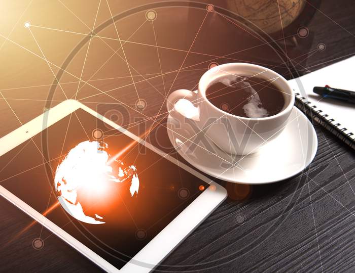 Tablet And Black Coffee On Wooden Table With Digital Earth World Map And Orange Light And Line Dot, Notebook And Pen, Technology Concept, Drinking And Relax Concept, Coffee Break Time Concept