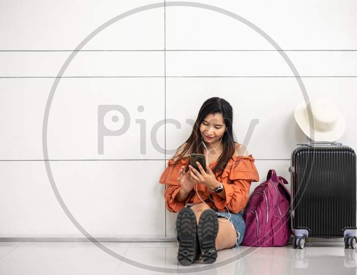 Asian Female Traveler Waiting For Flight And Using Smart Phone Outside Lounge In Airport. Travel And People Lifestyle Concept. Transportation And Passenger Theme.