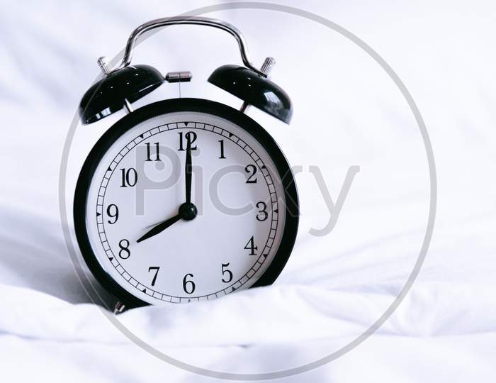 Black Alarm Clock On White Bed. Time And Hours Concept. Interior And Object Theme