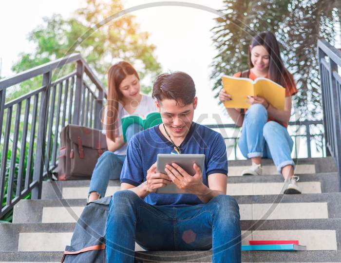 Group Of Asian College Student Reading And Reviewing By Textbook And Laptop At Stair At University. Technology And Education Learning Concept. Entertainment And Edutainment Theme.