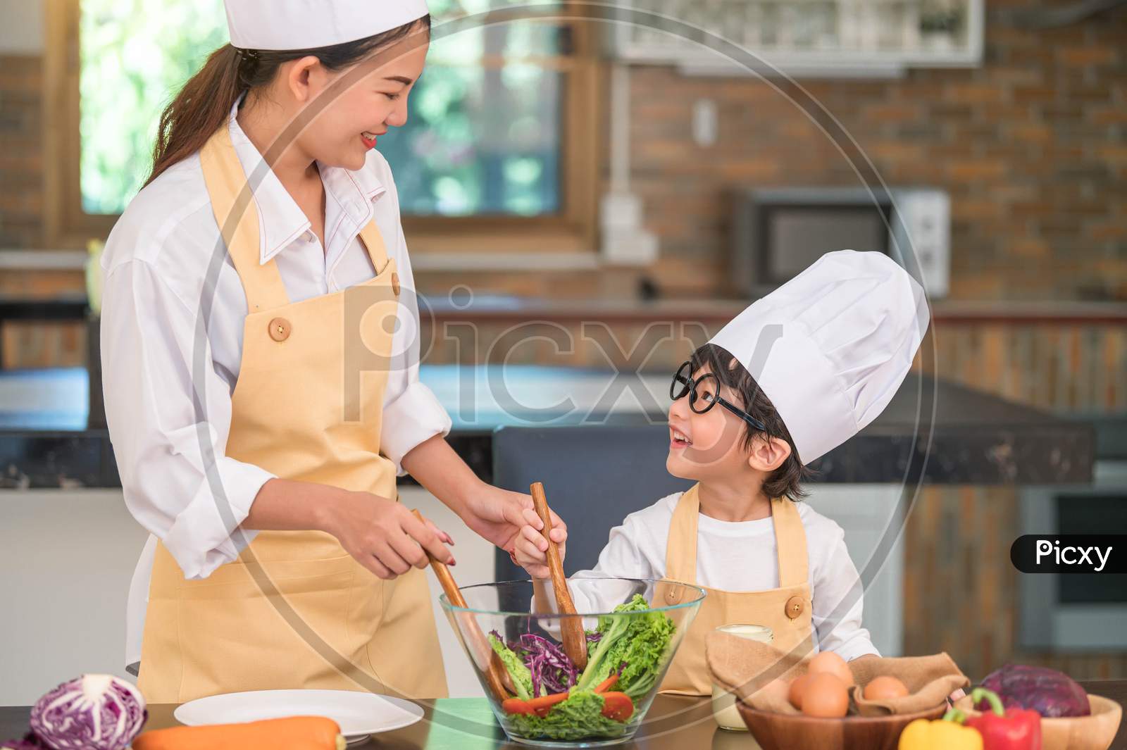 Happy Beautiful Asian Woman And Cute Little Boy With Eyeglasses Prepare To Cooking In Kitchen At Home. People Lifestyles And Family. Homemade Food And Ingredients Concept. Two Thai People Life