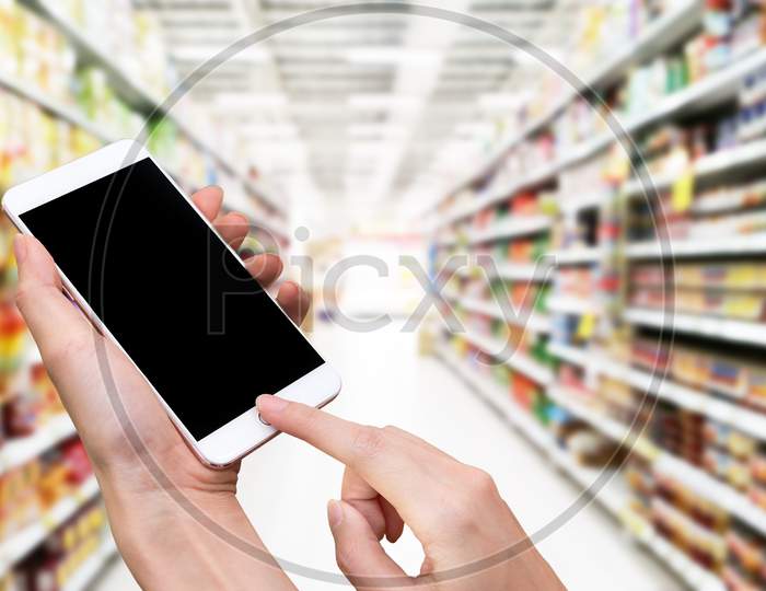 Woman Hold Smart Phone And Touch Button By Hand With Blank Screen For Advertisement, Blurry Supermarket Background ,Technology And Online Shopping Concept