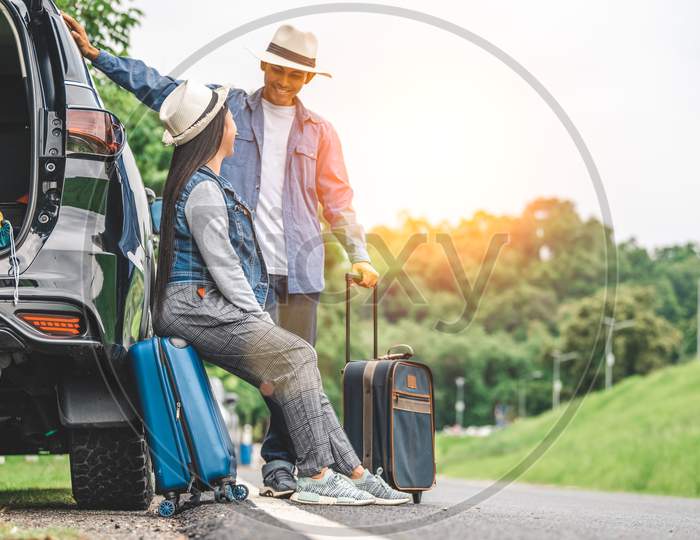 Closeup Lower Body Of Asian Couple Relaxing On Suv Car Trunk With Yellow Trolly Luggage Along Road Trip With Mountain Hill Background. Freedom Road Life. People Lifestyle And Transportation Travel