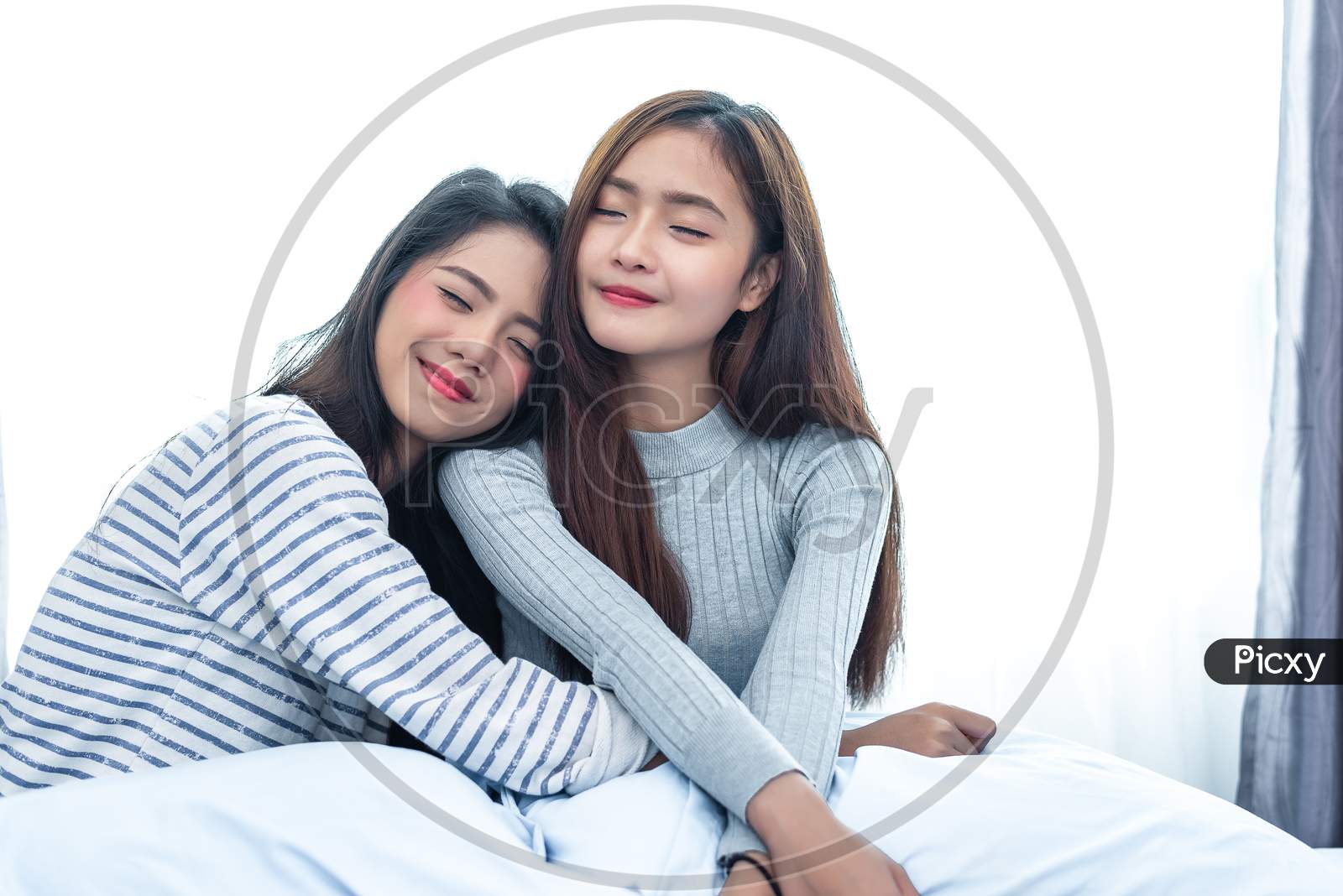 Two Asian Lesbian Hug Together In Bedroom. Beauty Concept. Happy Lifestyle And Home Sweet Home Theme. Cushion Pillow Element And Window Curtain Background. Love Scene Of Lovers