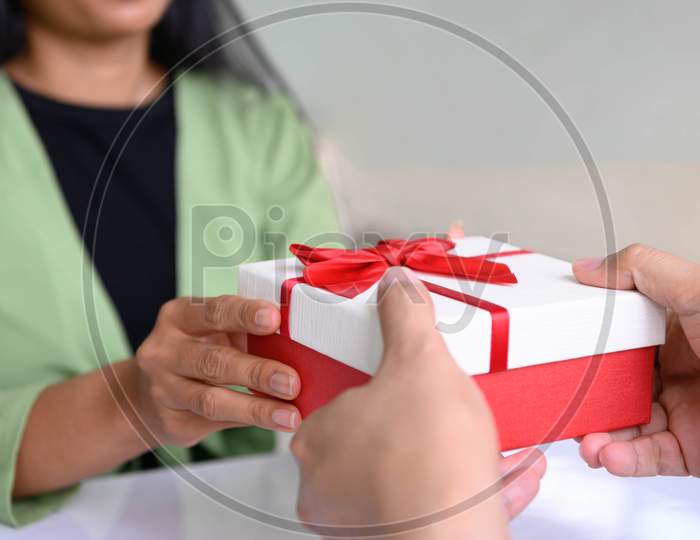 Closeup Of Hands Giving Gift Box In Christmas Day And New Year Festival To Each Other With Woman Background. Holiday And Event. Surprising Giftbox In Dating On End Year Party. People Lifestyle Concept