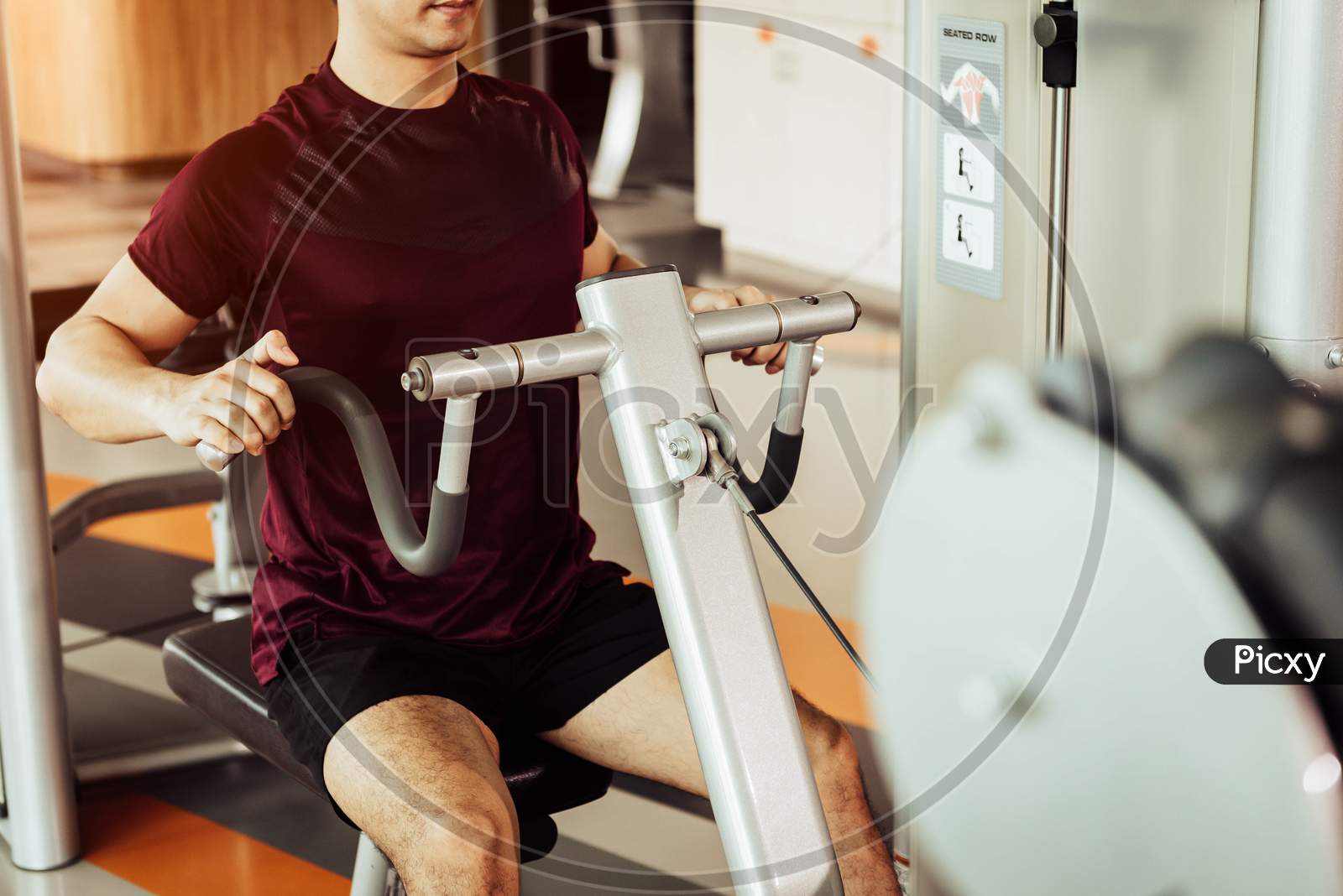 Front View Of Sport Man Using Back Muscle Stretch Machine Called Seated Row In Fitness Gym. People Lifestyles And Sport Workouts Concept. Close Up View