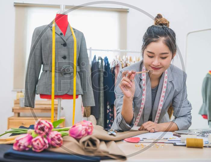 Attractive Asian Female Fashion Designer  Working In Home Office Workshop. Stylish Fashionista Woman Creating New Cloth Design Collection. Tailoring And Sewing. People Lifestyle And Occupation Concept