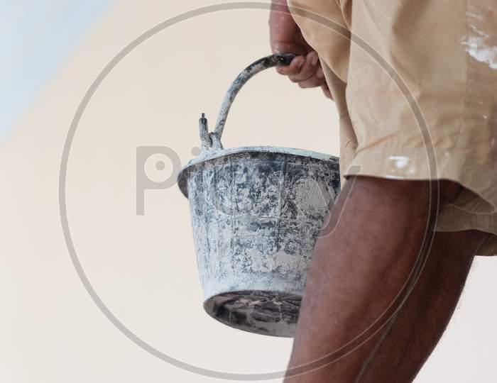 Close Up Of Black Paint Bucket And Painter Legs. Architecture And Civil Engineering Concept. Structure And Construction. Occupation And Job