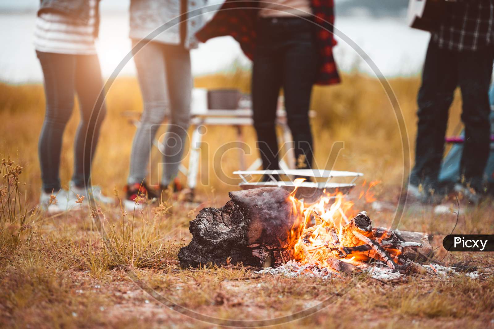 Closeup Of Campfire With Friendship Dancing To Beat Of The Music For Celebrating In Party With Mountain Meadow And Lake View Background. People Lifestyle And Travel Vacation. Picnic And Camping Tent