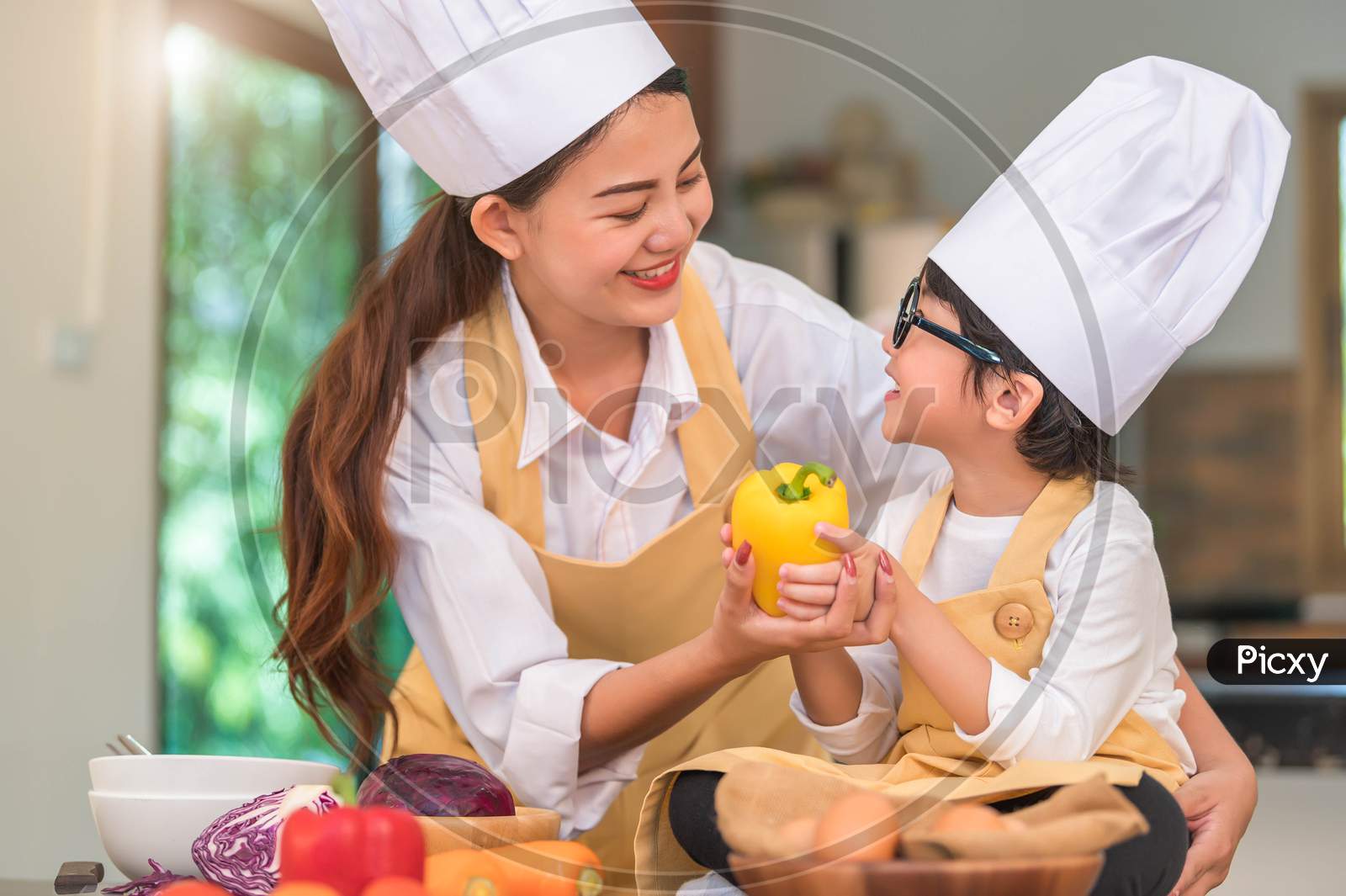Happy Beautiful Asian Woman And Cute Little Boy With Eyeglasses Prepare To Cooking In Kitchen At Home. People Lifestyles And Family. Homemade Food And Ingredients Concept. Two Thai Looking Each Other