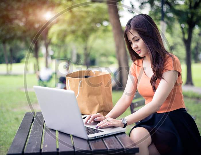 Asian Woman Using And Typing On Laptop Keyboard In Outdoors Park. Woman Chatting To Her Friends On Social Network. People And Lifestyle Concept. Nature And Technology Theme.