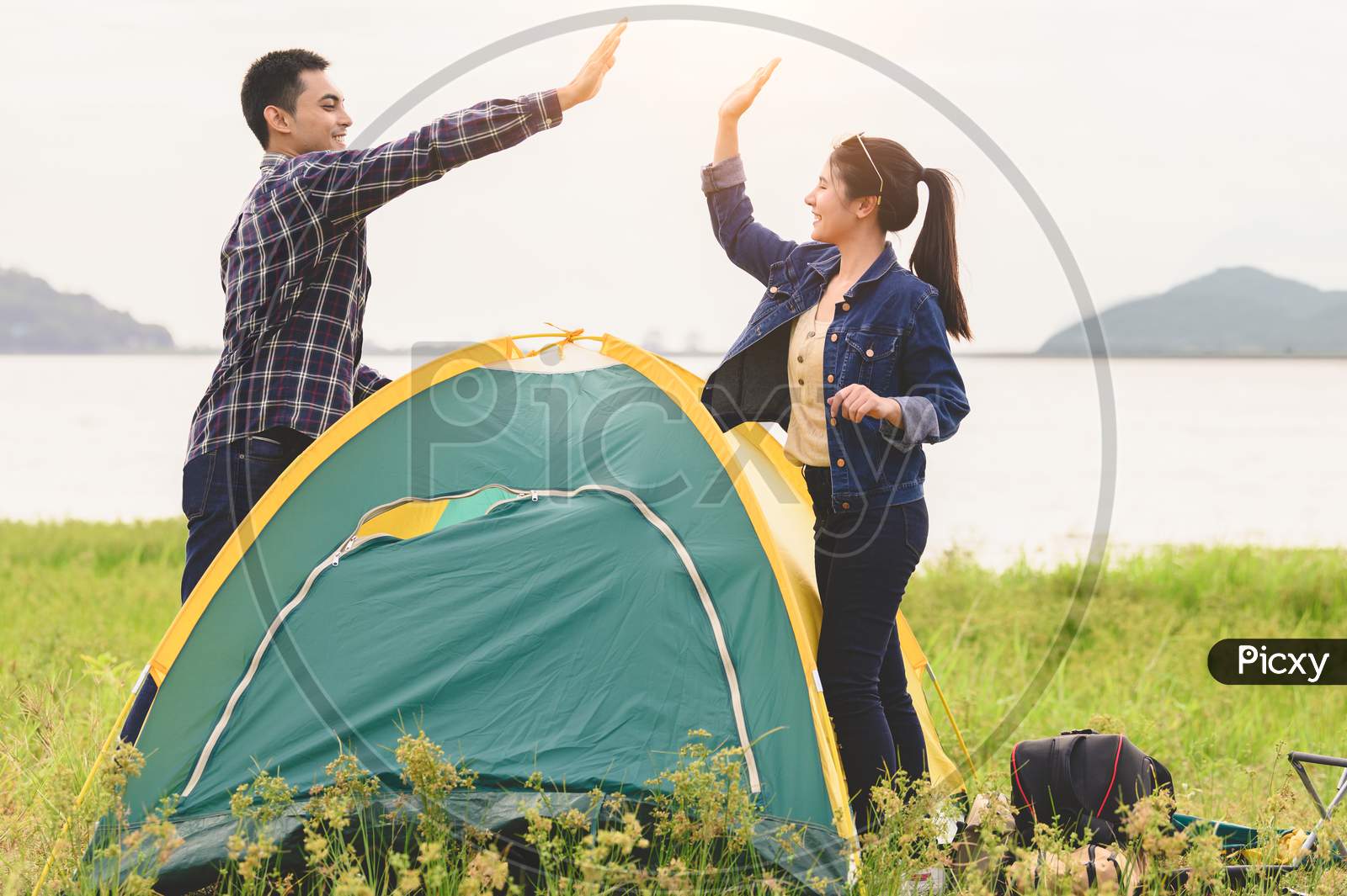 Two Asian Couples Finished Pitch And Doing High Five For Stay In Camping Tent  Meadow Overnight Honeymoon Picnic. People Lifestyle And Valentine Day Love Concept. Nature Travel Relaxation Activity