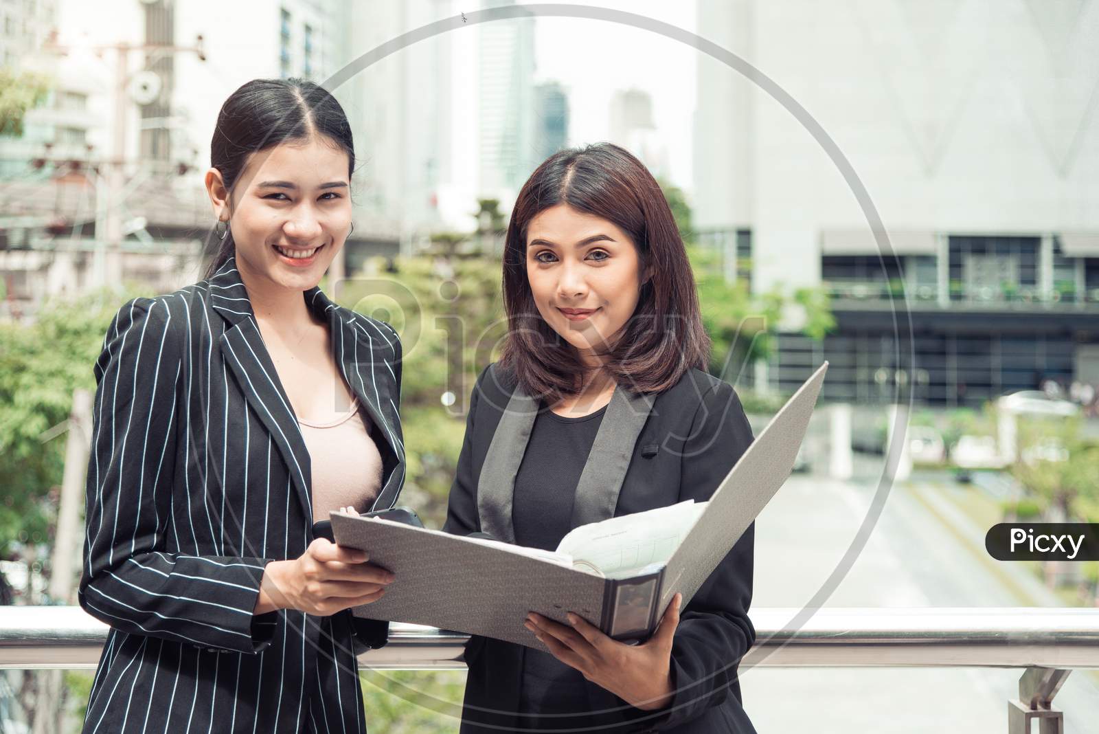 Two Young Asian Businesswomen Looking Into Document File Folder For Analyzing Profit Or Sale Break Even Point After Marketing. Business Teamwork Employees Of Lifestyle Working Women Concept.