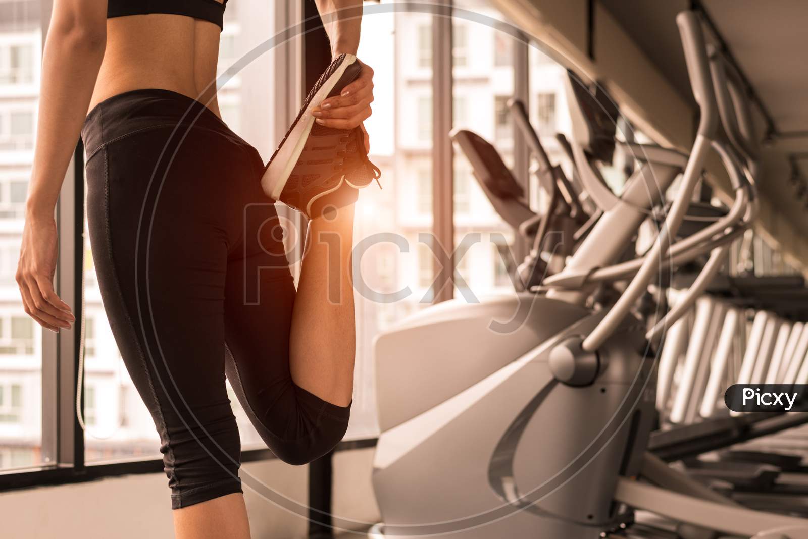 Close Up Beauty Woman Stretching Legs In Workout Fitness Gym Center With Sport Equipment And Treadmill Background. Sporty Girl Warming Up Before Exercise Training. Lifestyle And Healthy People Concept