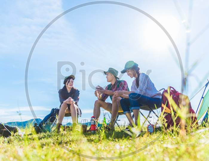 Group Of Travelers Camping And Doing Picnic In Meadow Field Foreground. Mountain And Lake Background. People And Lifestyles Concept. Outdoors Activity And Leisure Theme. Backpacker And Hiker Lifestyle