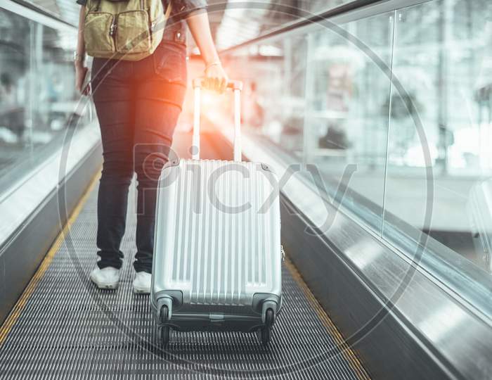 Back View Of Beauty Woman Traveling And Holding Suitcase On Escalator In Airport. People And Lifestyles Concept. Travel Around The World Theme. Adventure And Business Trip. Close Up  Lower Body Legs