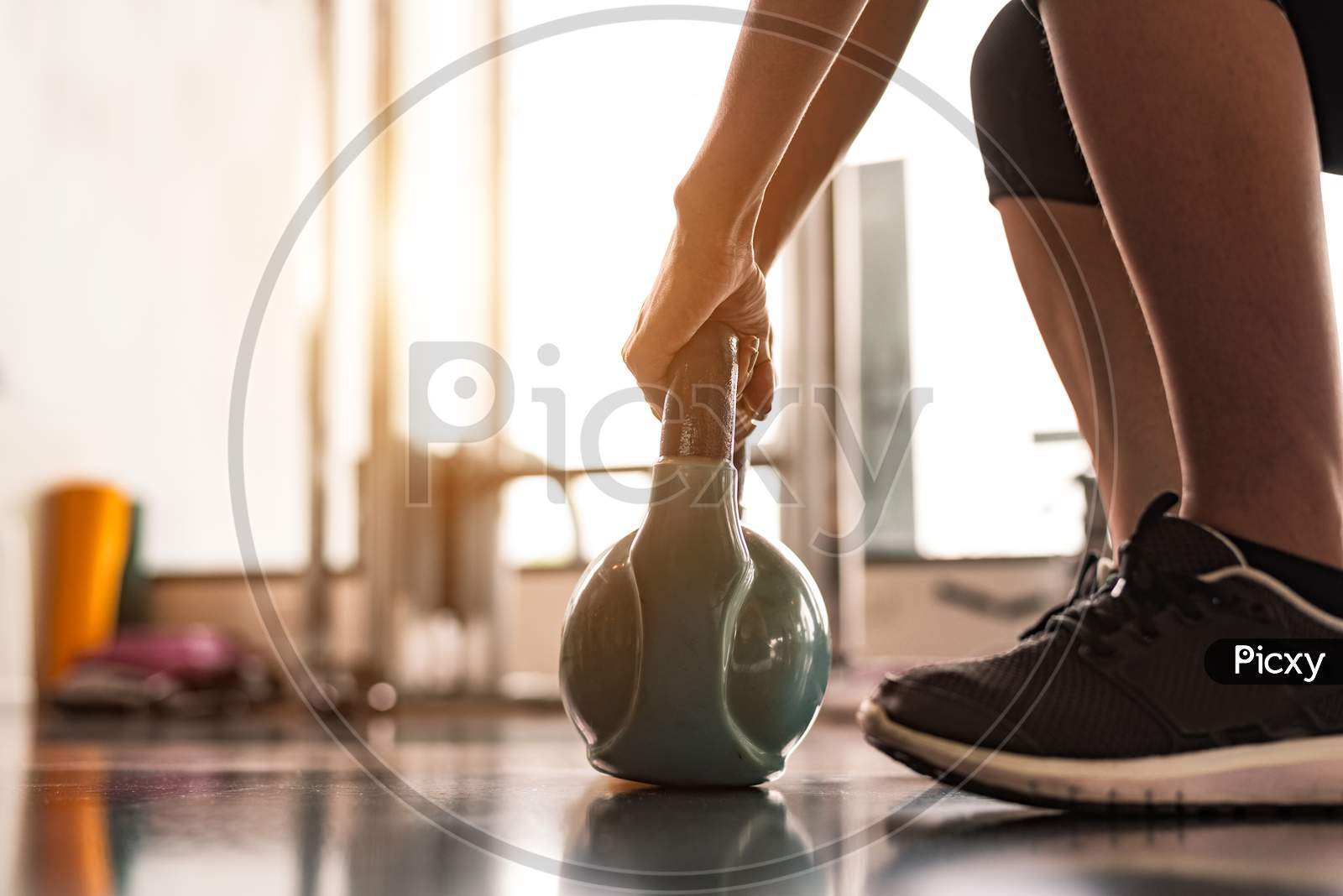 Close Up Of Woman Lifting Kettlebell Like Dumbbells In Fitness Sport Club Gym Training Center With Sport Equipment Near Window Background. Lifestyles And Workout Exercise For Bodybuilding And Healthy