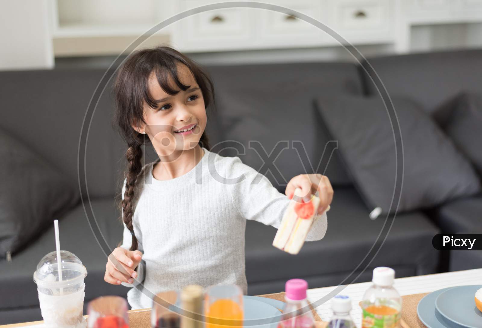 Happy Little Girl Giving Sandwich Cooking Toy As Chef In Living Room. Playful Of Child And Happiness Education And Development Concept. Learning And Leisure Of Cute Girl. Nursery And Daycare Theme.