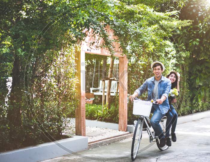 Happy Couple Riding Bicycle Together In Romantic View Park Background. Valentine'S Day And Wedding Honeymoon Concept. People And Lifestyles Concept.