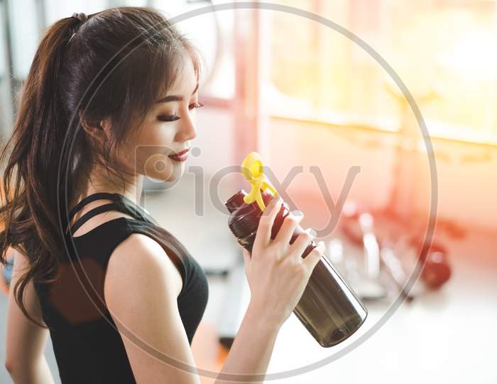 Asian Beautiful Woman Drinking Protein Shake Or Drinking Water In Sport Fitness Training Gym. Sports And People Concept. Fitness And Workout Theme.  Sun Flare Effect